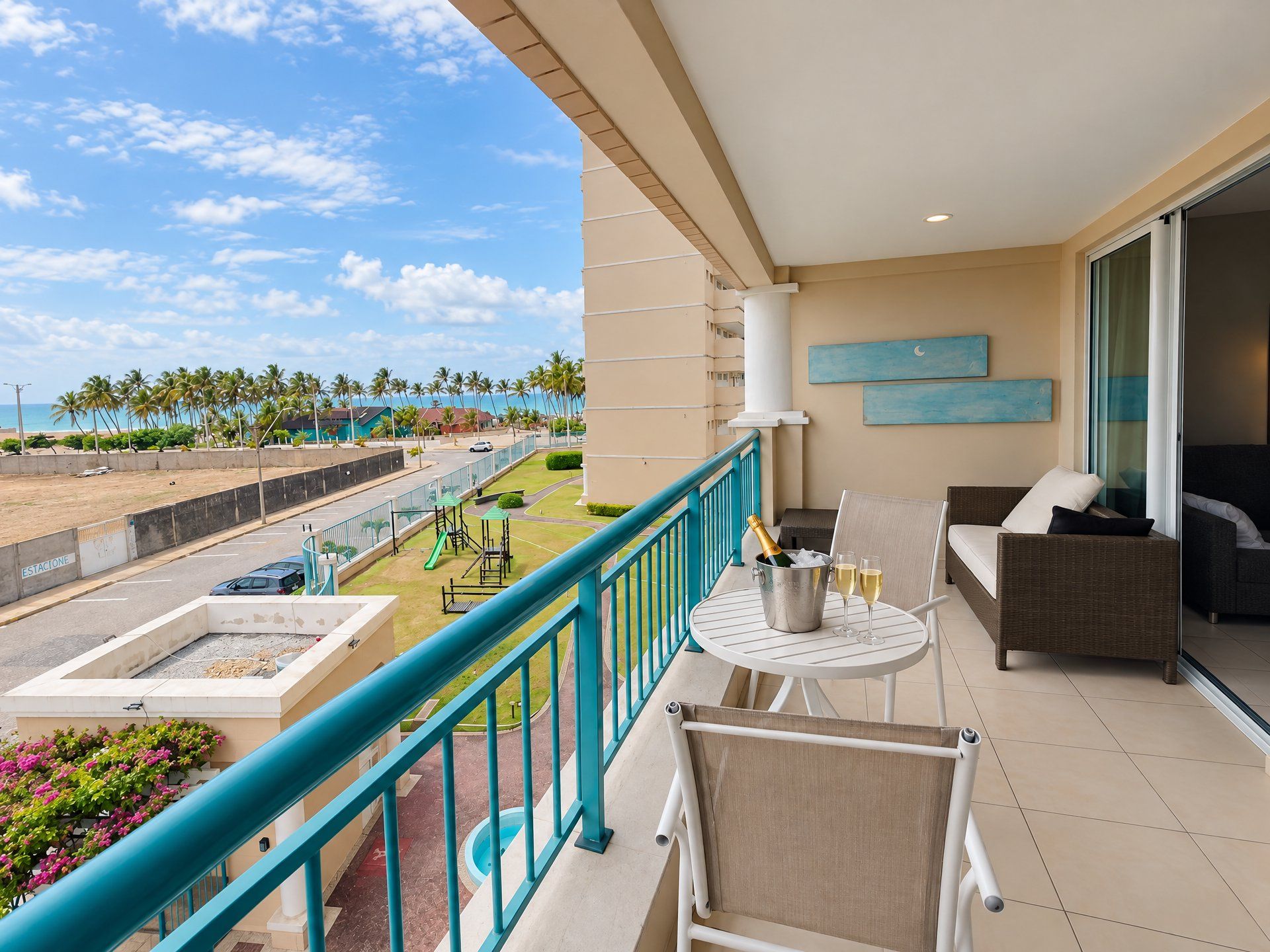 A balcony with a view of a beach, a pool, and a children's play area.