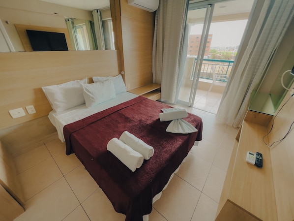 A hotel room with a bed, a red bedspread, white pillows, a white towel, a bedside table, a mirror, and a view of the outside. - Beach Village sea View 2 Bedrooms (Fortaleza)