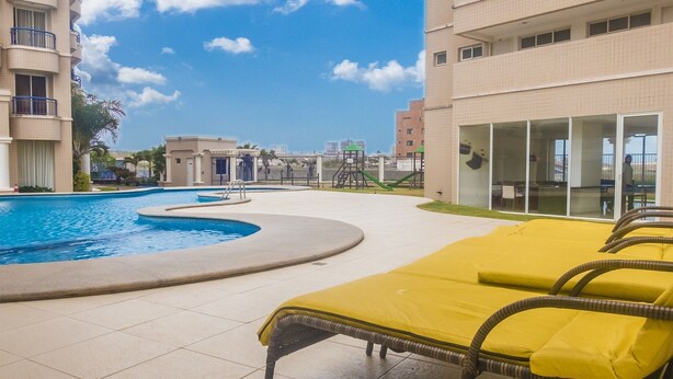 A swimming pool with lounge chairs, a children's play area, and a building with balconies. - Beach Village sea View 2 Bedrooms (Fortaleza)