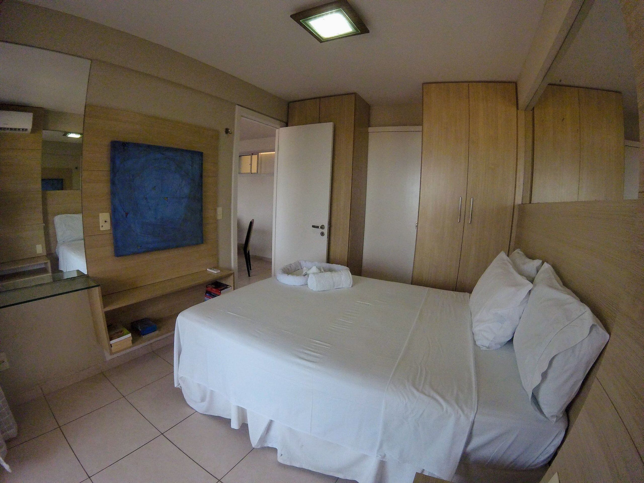 Quarto de hotel com uma cama, um guarda-roupa, uma mesa com cadeira e um espelho.