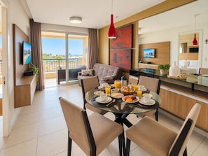 A modern hotel room with a balcony, a dining area with breakfast, and a television. - Beach Village sea View 2 Bedrooms (Fortaleza)