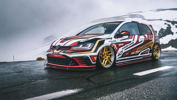 A customized sports car parked on a wet road with snow-capped mountains in the background.