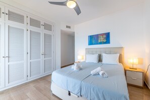 Ein ordentlich eingerichtetes Schlafzimmer mit einem Bett, Nachttischlampen, einem Deckenventilator und einem an der Wand hängenden Kunstwerk.
