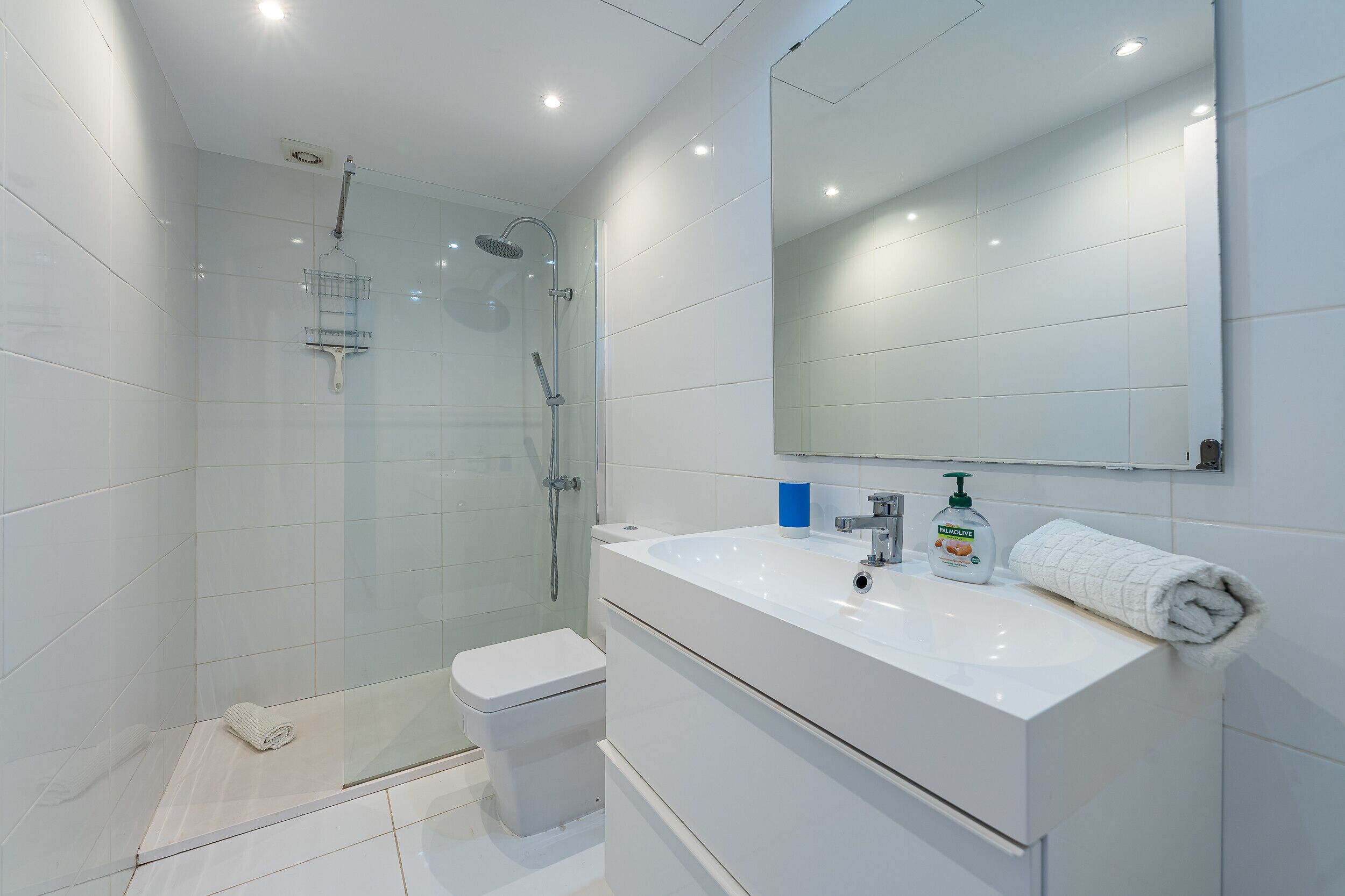 A modern bathroom with a glass shower enclosure, a white sink with a mirror above it, and a toilet.