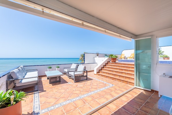 A balcony with outdoor furniture, a view of the sea, and a staircase leading to an upper level. - Arkadia – Beachfront Penthouse with Private Pool (Mijas Costa)