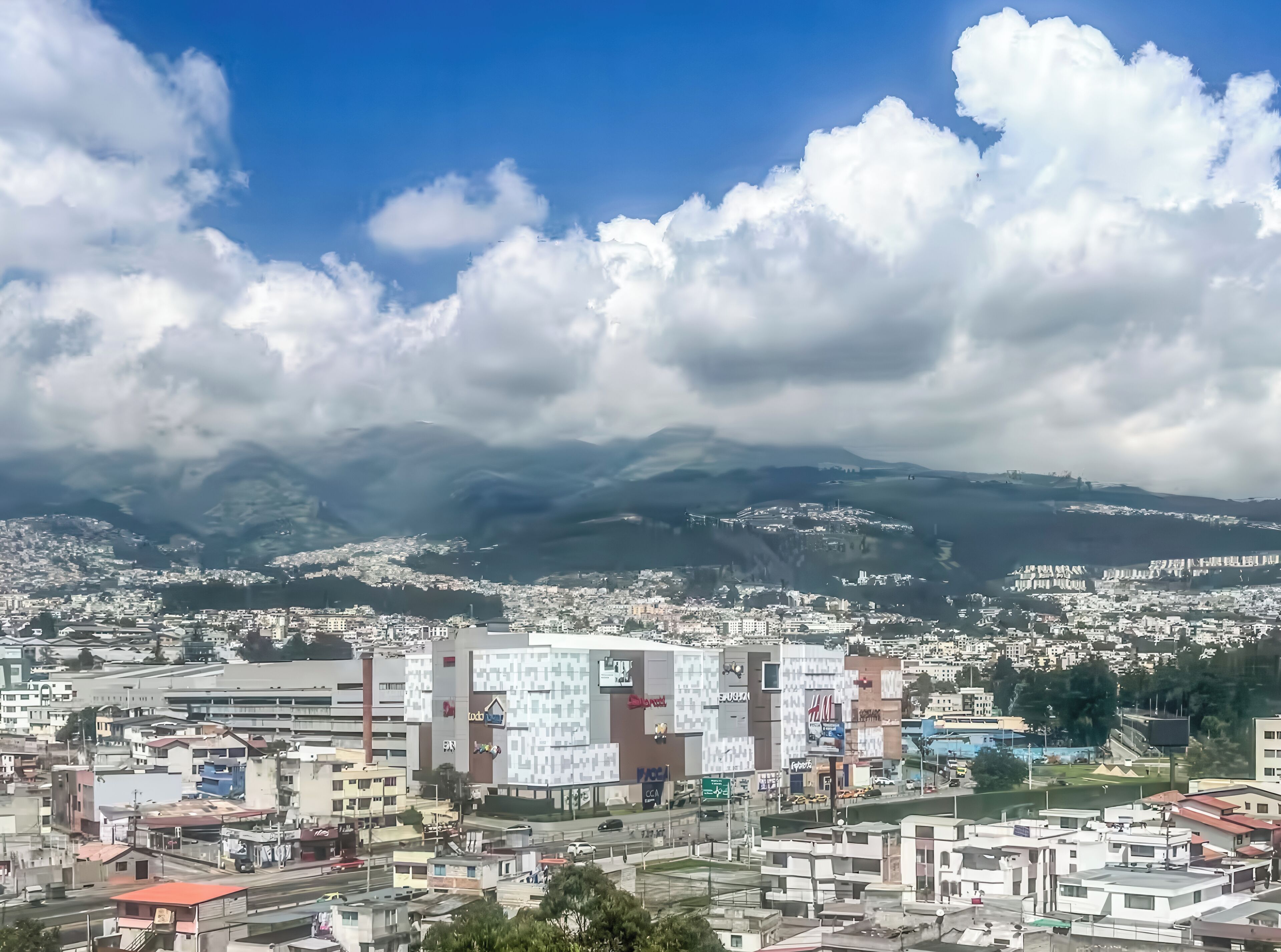 Un paisaje urbano con un edificio destacado que presenta un gran panel publicitario digital, rodeado de zonas residenciales y montañas al fondo.