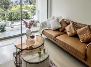 A modern living room with a leather sofa, a glass coffee table, and a view of a green landscape through large windows. - Blaze 1 (Quito)