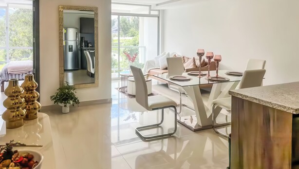 Un comedor moderno con una mesa de vidrio, sillas blancas y vistas al exterior.
