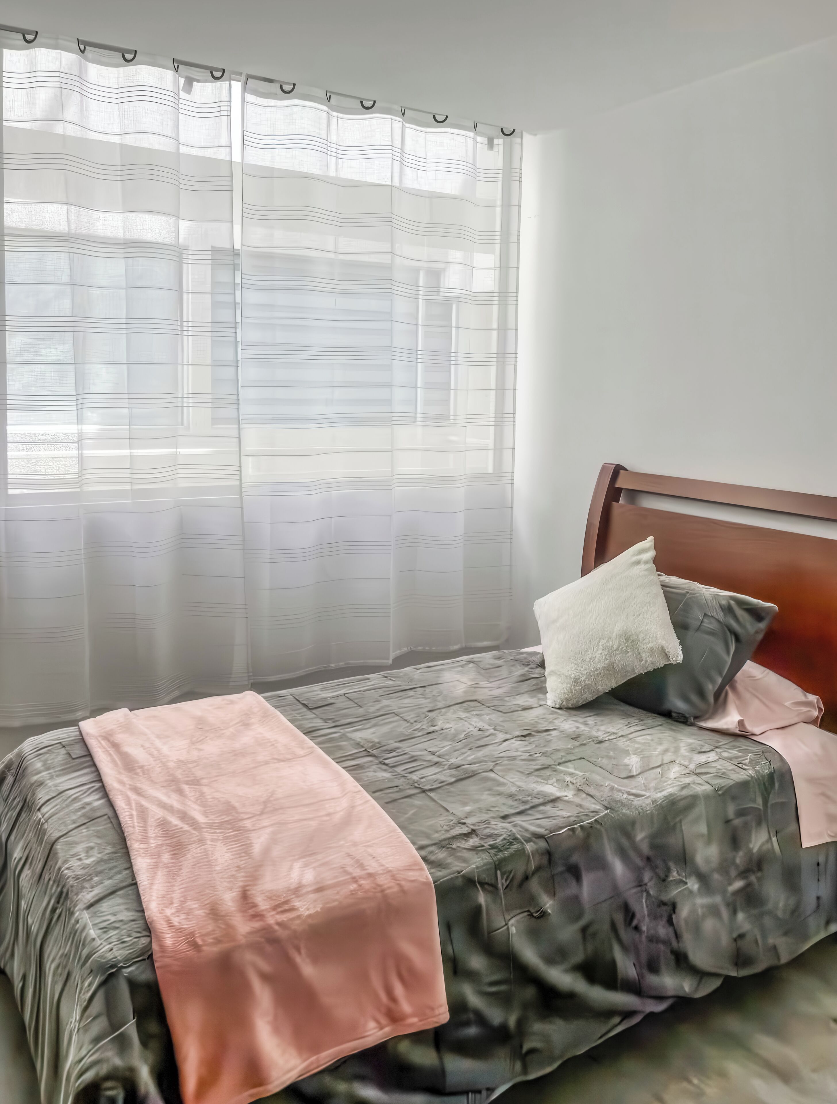 A bed with a headboard, a pink blanket, and two pillows.