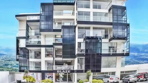 Un edificio de varios pisos con balcones, un letrero que dice 'BLAZE' y coches estacionados al frente.
