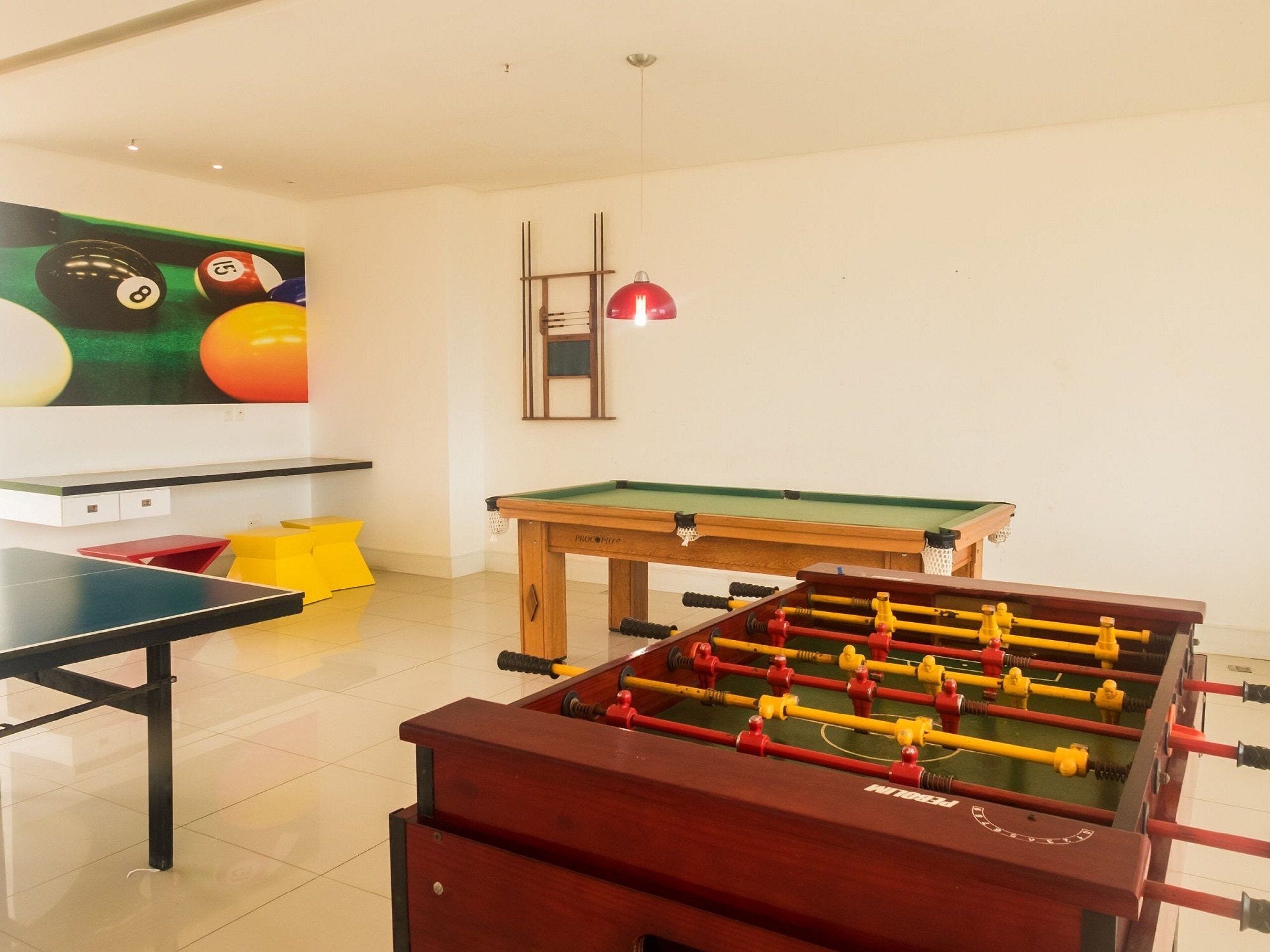 A room with a foosball table, a pool table, and a billiards table.