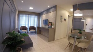 Un salon moderne comprenant un canapé, deux fauteuils, une table à manger avec des chaises, une plante en pot et un téléviseur fixé au mur.