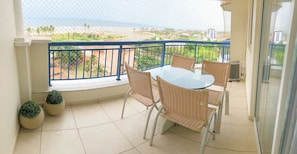 Ein Balkon mit Glastisch und Korbstühlen, mit Blick auf Strand und Stadtbild.