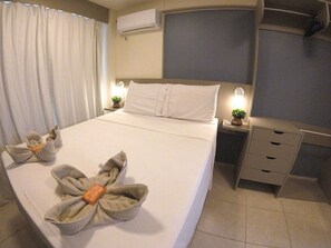 Ein Hotelzimmer mit einem Bett, Nachttischen, einer Klimaanlage, einem Schreibtisch und einem Sessel.
