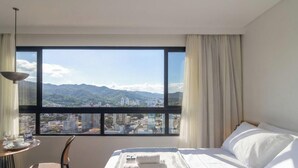 Una habitación de hotel con un ventanal grande, una cama, una mesa con un vaso y una silla.
