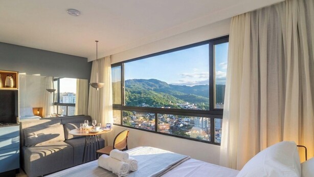 Habitación de hotel con cama, mesa de comedor, sofá y vistas a la ciudad y montañas.