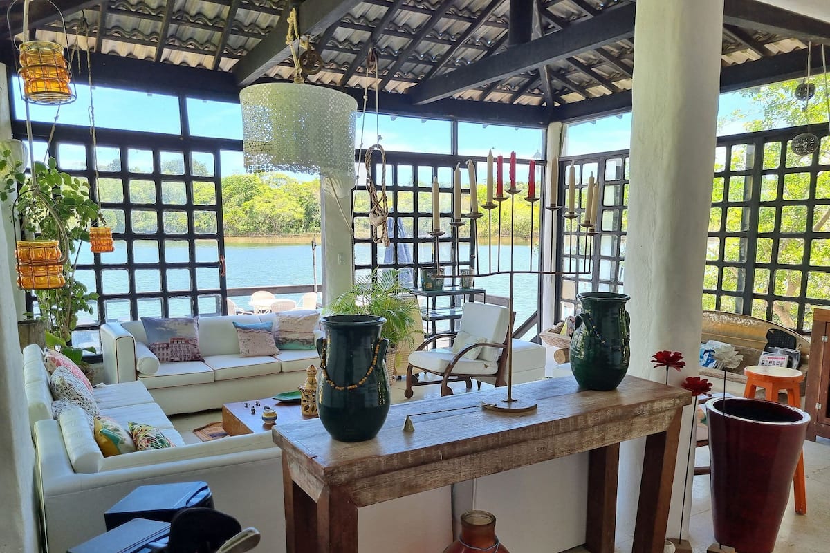 A room with a sofa, a table with vases, and a view of a body of water through large windows.
