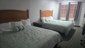 A hotel room with two beds, a nightstand, a window with curtains, and a patterned carpet. - Cajun Inn  (Shreveport)