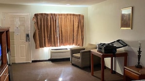 A hotel room with a bed, a desk with a suitcase, a chair, a coat rack, a door, and a window with curtains. - Cajun Inn  (Shreveport)