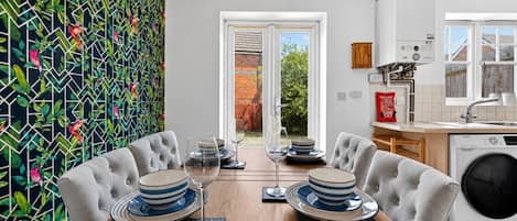 Un comedor con una mesa dispuesta para dos, una cocina con lavadora y vistas al exterior a través de un ventanal.
