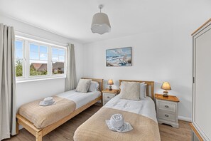 Quarto com duas camas de solteiro, um quadro, uma janela com cortinas e uma mesa de cabeceira com abajur.