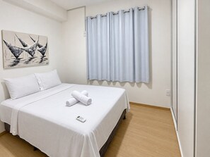 Une chambre d’hôtel avec un lit, du linge de lit blanc, un tableau au mur et une fenêtre avec des rideaux.