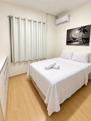 A hotel room with a bed, a window with curtains, an air conditioning unit, and a painting on the wall. - Apartamento Novinho 2 Quartos e Vista mar (Fortaleza)