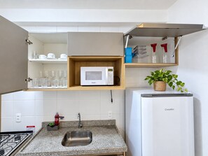 A compact kitchen with a built-in microwave, a sink, and a small refrigerator. - Apartamento Novinho 2 Quartos e Vista mar (Fortaleza)