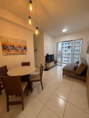 Un soggiorno con tavolo da pranzo, sedie, divano, televisione e un quadro appeso al muro.