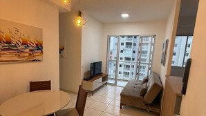 Ein Wohnzimmer mit Esstisch, Stühlen, einer Couch, einem Fernseher und einem Gemälde an der Wand.