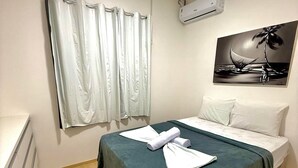 Ein Hotelzimmer mit Bett, Gemälde, Klimaanlage und einem Fenster mit Vorhängen.