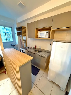 A compact kitchen with a wooden island, stainless steel appliances, and a view of a building outside. - Apartamento Novinho 2 Quartos e Vista mar (Fortaleza)