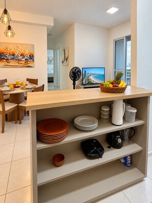 Una cocina moderna con comedor, un televisor mostrando una escena de playa y una cesta de fruta sobre la encimera.