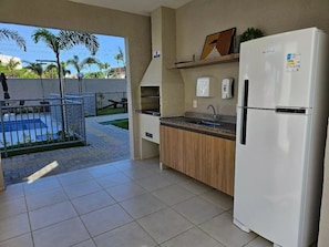 A kitchen with a refrigerator, a sink, and a countertop. There is a view of a pool outside. - Apartamento Novinho 2 Quartos e Vista mar (Fortaleza)