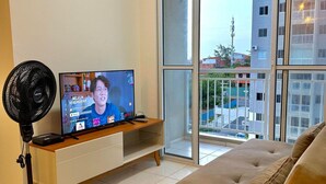 Ein Wohnzimmer mit Fernseher, Ventilator, einer Couch und einer Glastür zum Balkon.