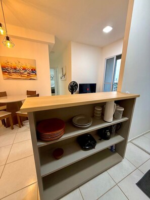 A modern kitchen with a wooden countertop, shelves with dishes, a fan, and a painting on the wall. - Apartamento Novinho 2 Quartos e Vista mar (Fortaleza)