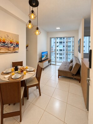 Una sala de estar moderna con comedor, un sofá, un televisor y un amplio ventanal con vistas a la ciudad.