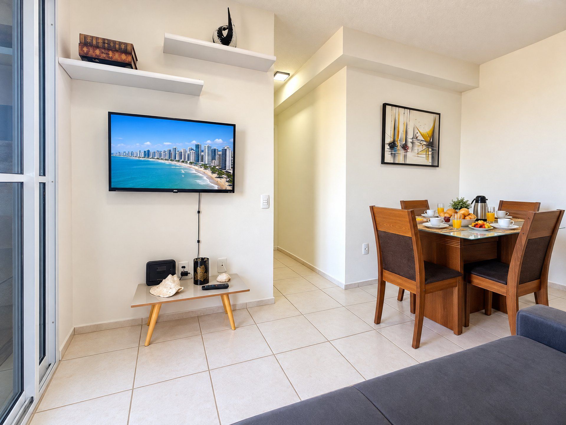 Una sala moderna con televisor de pantalla plana, una mesa de comedor con sillas y una mesa de centro con un control remoto, libros y un objeto decorativo.