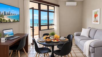 Una sala de estar moderna con comedor, una computadora portátil sobre un escritorio y vista al mar a través de amplios ventanales.