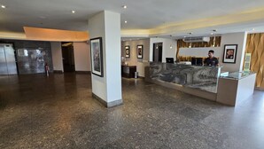 A hotel lobby with a reception desk, framed artwork, a refrigerator, and a bench. - Golden Flat By Fortaleza Temporada (Fortaleza)
