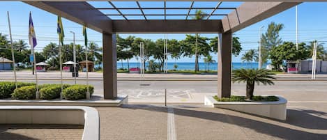 A covered pedestrian area with a view of the sea, a kiosk, and flags.