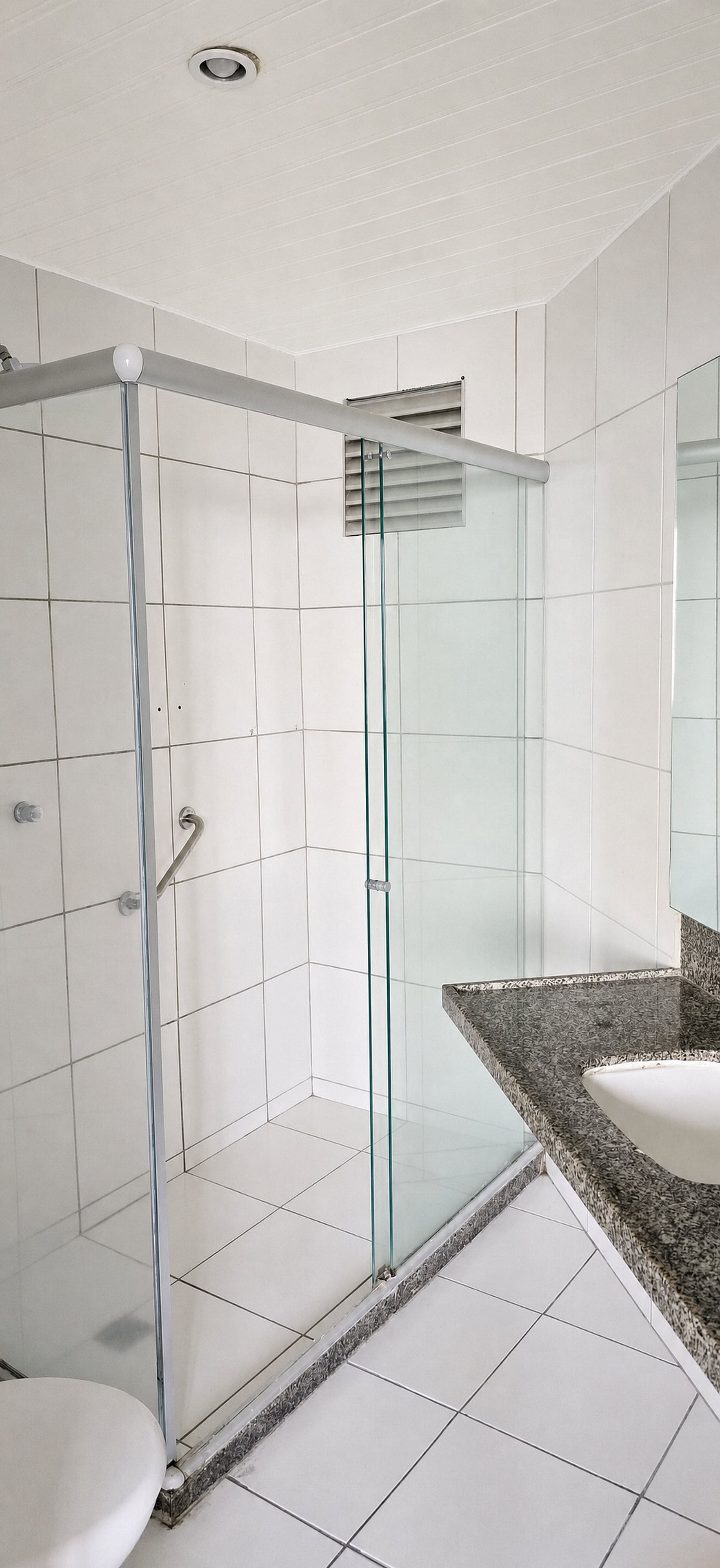 A modern bathroom with a glass shower enclosure, white tiled walls, and a granite countertop.