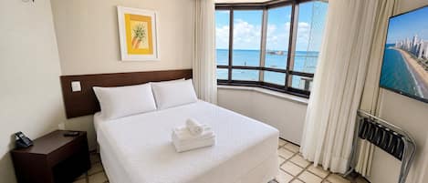 Habitació d'hotel amb un llit, una taula de nit, un comandament a distància, un quadre amb marc, una finestra amb vista al mar i una televisió penjada a la paret.