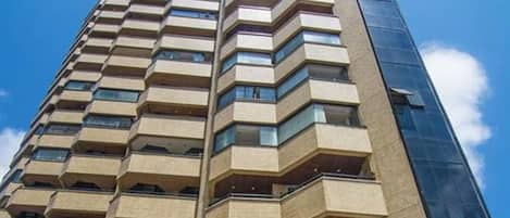 A high-rise building with a pool at the base, featuring multiple balconies and a modern architectural design.