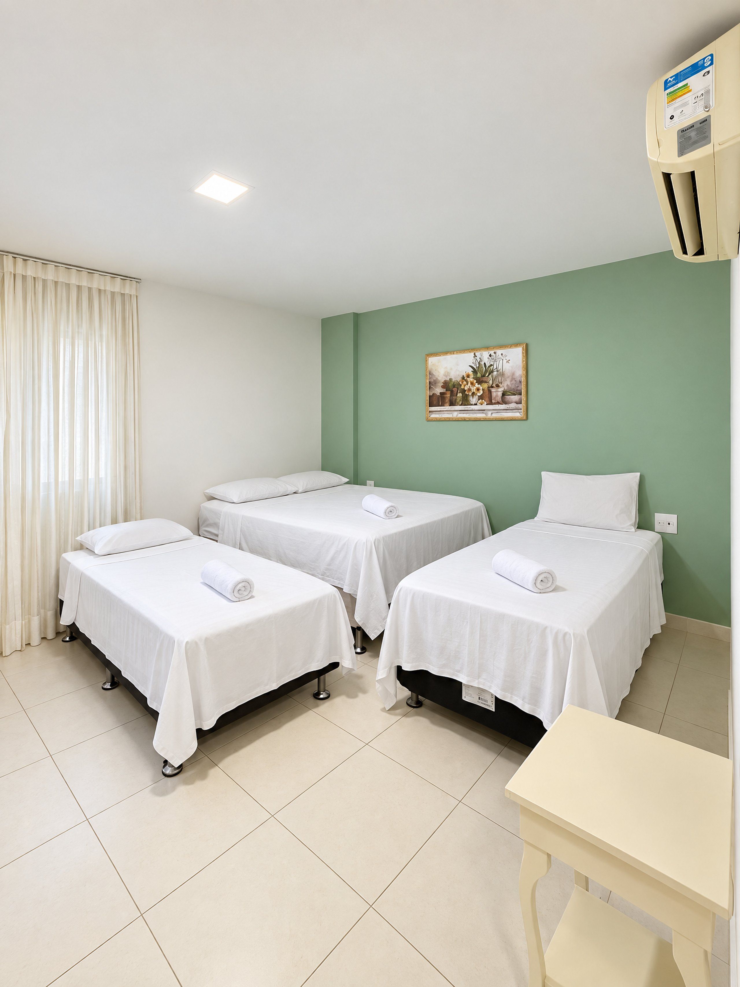 A hotel room with three single beds, a small table, and a painting on the wall.