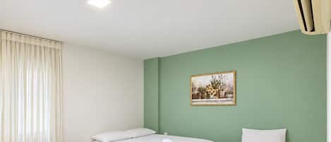 A hotel room with three single beds, a small table, and a painting on the wall.