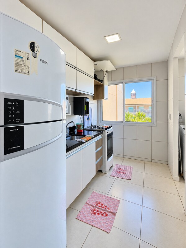 Cozinha moderna com armários brancos, forno embutido e janela com vista para um edifício.