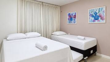 Quarto de hotel com duas camas, uma cortina e dois quadros florais na parede.