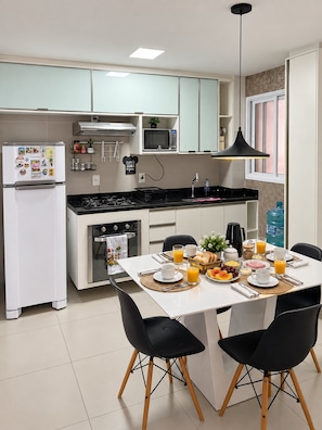 Une cuisine moderne avec des meubles blancs, un four à micro-ondes, une cuisinière et un coin repas avec une table mise pour le petit-déjeuner.