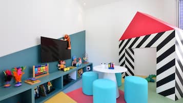 A children's playroom with a TV, toys, a table, and colorful seating.